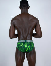 A man viewed from behind wearing green patterned briefs with a gray waistband, standing against a light gray studio background.