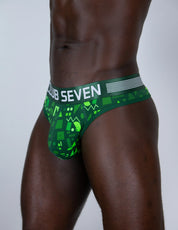 A close-up of a male model wearing green patterned thongs with a white waistband that reads 'CLUB SEVEN'.