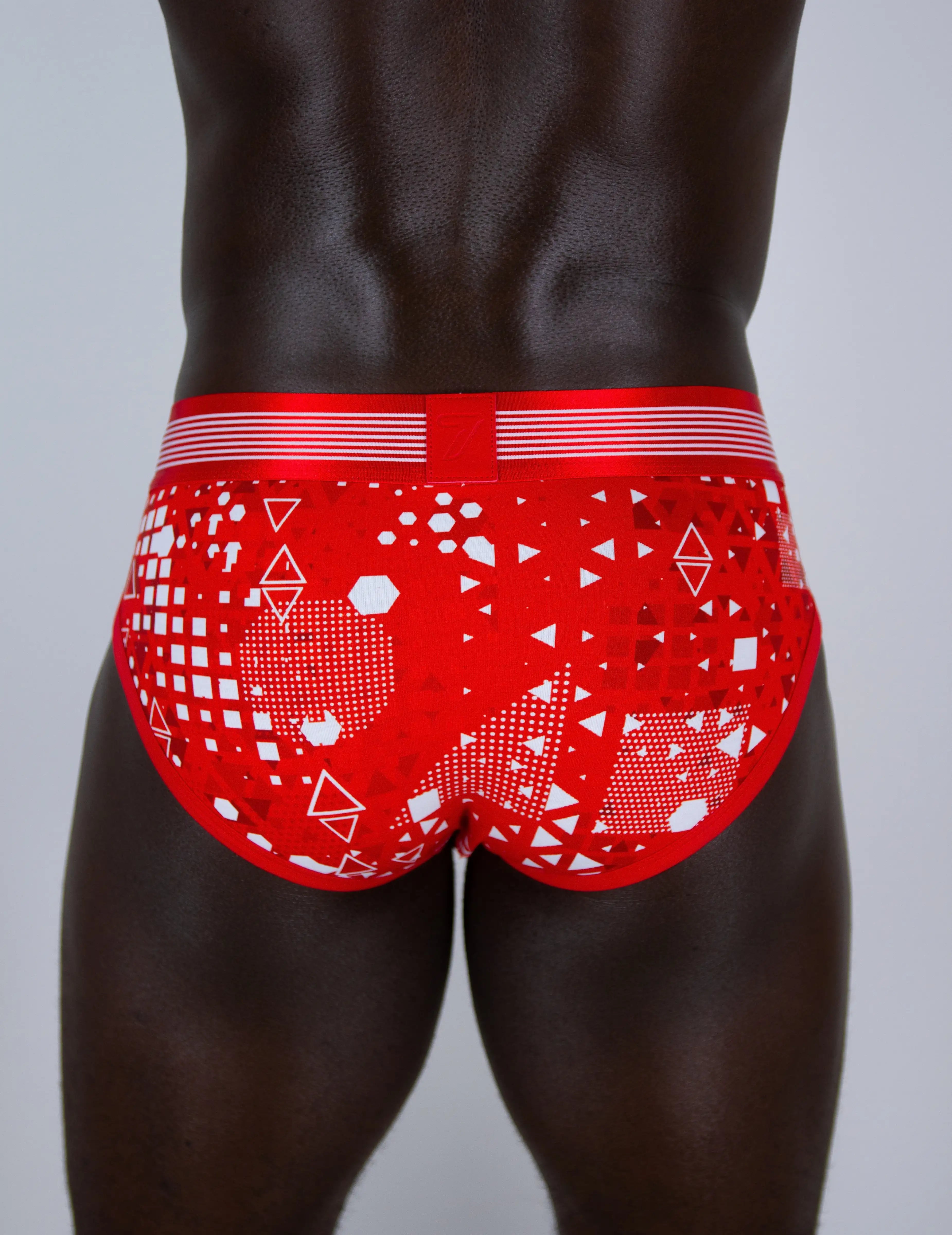 Red men's briefs underwear with a white geometric pattern, shown from the back on a male model against a light grey background.