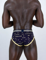 Rear view of a muscular man wearing navy blue boxer briefs with gold star patterns and a gold trim, on a light gray background.