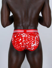 Rear view of a man wearing red and white patterned sports briefs against a light gray studio background.